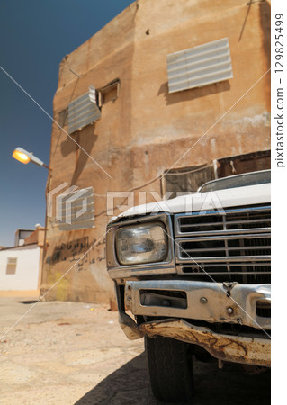Close-Up of Old White Pickup Truck in Front of Rustic Building, Saudi Arabia 129825499