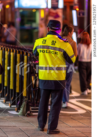 A police officer in a yellow jacket stands on a busy street at night in Seoul, South Korea 129825957