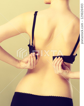 Woman dressing up her bra rear view 129826493