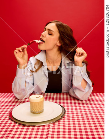 Woman tasting whipped cream on chili pepper with playful expression against red background Woman tasting whipped cream on chili pepper with playful expression against red background 129826704