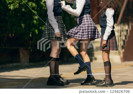 Schoolgirls playing traditional jumping elastic band game with joyful energy 129826706