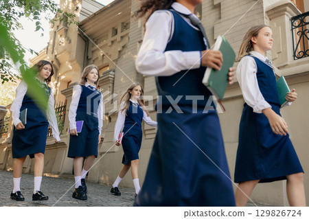 Schoolgirls in uniform walking along street with books in hands expressing determination 129826724