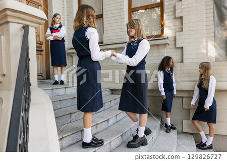 Group of schoolgirls interacting on stairs in uniform showing friendship and emotions Group of schoolgirls interacting on stairs in uniform showing friendship and emotions 129826727