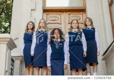 Confident schoolgirls in navy uniform posing together in front of building entrance 129826788