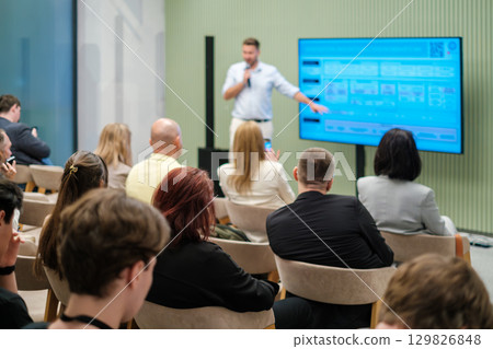 Audience listening to a speaker presenting on a screen in a modern room Audience listening to a speaker presenting on a screen in a modern room 129826848