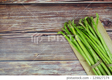 Bunch of fresh green asparagus stems with cutting wooden board on wooden background 129827174