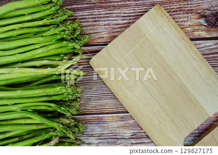 Bunch of fresh green asparagus stems with cutting wooden board on wooden background 129827175