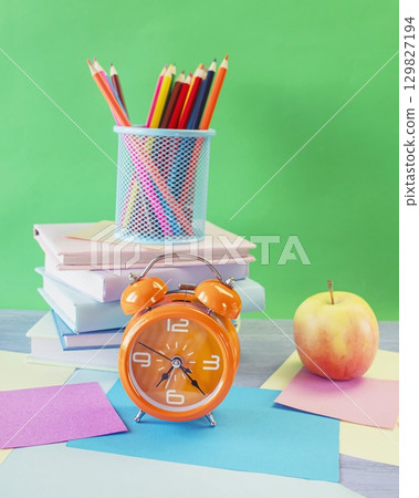 Back to school concept. Alarm clock, stack of books, apple, colored pencils and pastel colored paper on bright background. Back to school concept. Alarm clock, stack of books, apple, colored pencils and pastel colored paper on bright background. 129827194