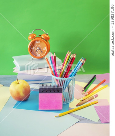 Back to school concept. Alarm clock, stack of books, apple, colored pencils and pastel colored paper on bright background. Back to school concept. Alarm clock, stack of books, apple, colored pencils and pastel colored paper on bright background. 129827196