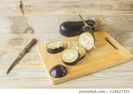 Fresh eggplants on cutting board and knife on wooden background, cooking fresh vegetables in kitchen, healthy food. Fresh eggplants on cutting board and knife on wooden background, cooking fresh vegetables in kitchen, healthy food. 129827341