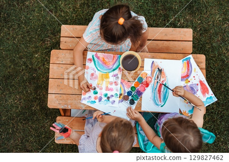 Children painting with watercolors at a wooden table in a garden Children painting with watercolors at a wooden table in a garden 129827462