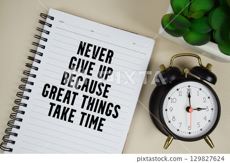 Never give up because great things take time text written on notepad with alarm clock 129827624