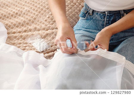 Woman attaching hooks to sheer white curtain for home decoration and room update project. 129827980