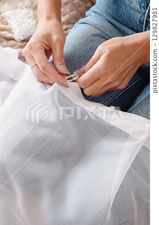 Woman attaching white curtain hooks to sheer fabric. Home decor and DIY project for living space. Woman attaching white curtain hooks to sheer fabric. Home decor and DIY project for living space. 129827981