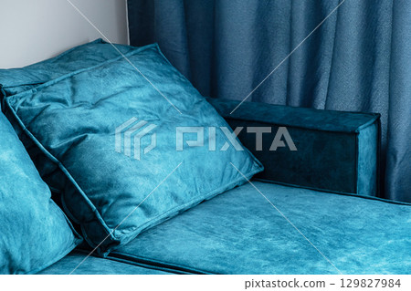 Close up of teal blue couch with fluffy pillows and matching curtains in cozy living room. Close up of teal blue couch with fluffy pillows and matching curtains in cozy living room. 129827984