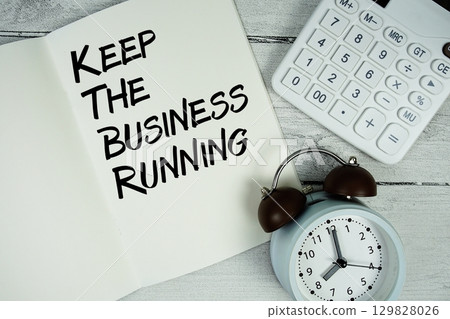 Keep The Business Running text on paper notebook page with alarm clock and calculator on wooden background 129828026