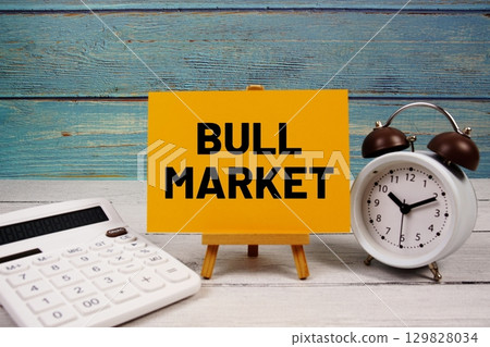 Bull Market text written on paper card with calculator and alarm clock on wooden background 129828034