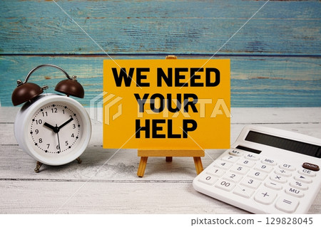 We Need Your Help text written on paper card with calculator and alarm clock on wooden background 129828045