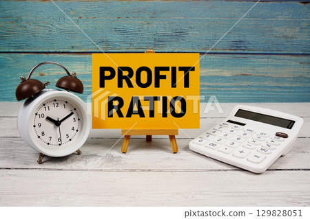 Profit Ratio text written on paper card with calculator and alarm clock on wooden background 129828051