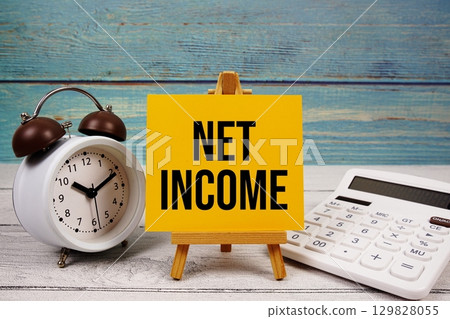 Net Income text written on paper card with calculator and alarm clock on wooden background 129828055