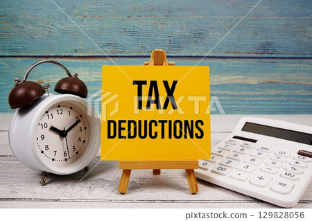 Tax Deductions text written on paper card with calculator and alarm clock on wooden background 129828056