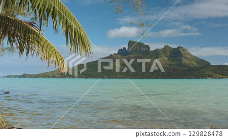 Verdant mount otemano rising from crystal-clear turquoise lagoon, framed by swaying palm leaves against cerulean sky with fluffy white clouds in French Polynesia's pristine landscape Verdant mount otemano rising from crystal-clear turquoise lagoon, framed by swaying palm leaves against cerulean sky with fluffy white clouds in French Polynesia's pristine landscape 129828478