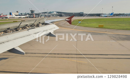 Airplane wing with open flaps approaching airport terminal 129828498