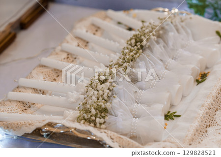 Stack of Wedding Favors: White Candles Decorated with Baby's Breath, Lace Cloth and Ribbon. Elegant Wedding Table Setting Details Stack of Wedding Favors: White Candles Decorated with Baby's Breath, Lace Cloth and Ribbon. Elegant Wedding Table Setting Details 129828521