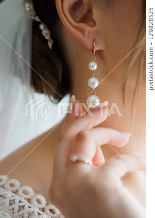 Elegant Bride Holding Pearl Earrings: Close-up Wedding Jewelry Shot, Soft White Lace, Delicate Pearls, Golden Metal, Romantic and Luxurious Style. Elegant Bride Holding Pearl Earrings: Close-up Wedding Jewelry Shot, Soft White Lace, Delicate Pearls, Golden Metal, Romantic and Luxurious Style. 129828525