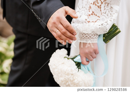 Romantic Wedding Ceremony Detail: Groom Putting Ring on Bride's Finger, White Bouquet, Formal Attire, Sunlight, Love, Celebration, Bridal Scene 129828586