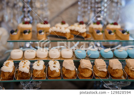 Elegant Wedding Dessert Table with Pastel Mini Cakes and Cream Puffs Displayed on Tiered Stands, Luxurious Celebration Concept 129828594
