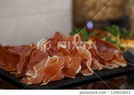 Elegant Prosciutto Platter: A Close-Up of Italian Cured Ham Slices Served on Slate with Arugula, Appetizers, Fine Dining, and Warm Tones 129828601