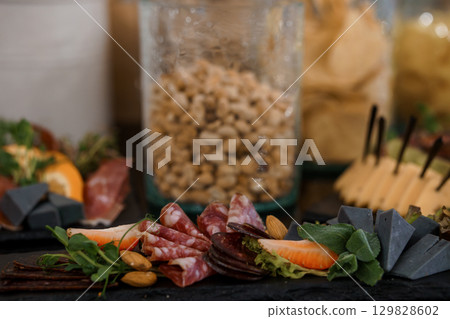 Elegant Charcuterie Display with Nuts, Cured Meats, Cheeses, and Slate Board. Dark Rustic Setting with Appetizers. 129828602