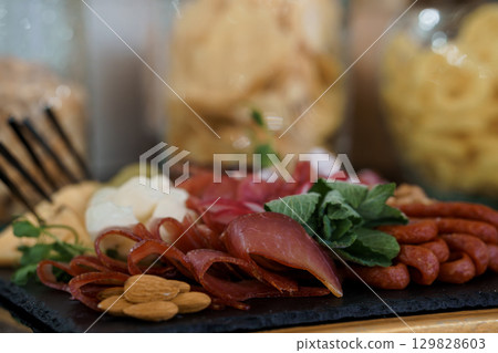 Charcuterie Board Assortment: Prosciutto, Salami, Almonds, Cheese, Herbs, Antipasto Platter, Wood Surface, Dark Tones, Gourmet Food Styling. 129828603