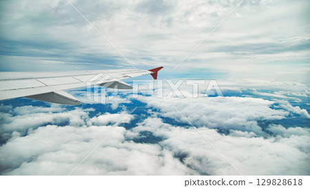 Airplane wing cutting through misty clouds, revealing expansive landscape during flight 129828618