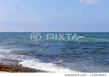 Blue sea with waves, clear weather, and a yacht far away. 129828641