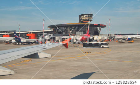 Airplane wing overlooking international airport runway, featuring terminal, control tower, parked aircraft. 129828654