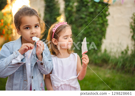 Little girls enjoying sweet treats in sunny garden Little girls enjoying sweet treats in sunny garden 129828661