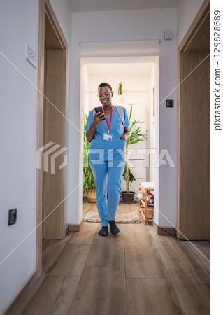 Young female doctor in blue scrubs using her smartphone at home 129828689