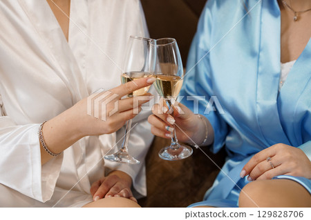 Two Women Toasting Champagne in Silk Robes, Luxury Lifestyle, Celebration, Golden Hues, Elegant Indoor Scene, Friendship, Wellness, Sparkling Wine. Two Women Toasting Champagne in Silk Robes, Luxury Lifestyle, Celebration, Golden Hues, Elegant Indoor Scene, Friendship, Wellness, Sparkling Wine. 129828706