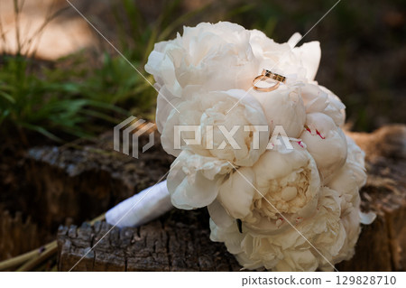 Wedding Rings on Peony Bouquet - Romantic Marriage Ceremony Symbolism with White Flowers, Gold Bands, Natural Forest Backdrop, Soft Focus Style Wedding Rings on Peony Bouquet - Romantic Marriage Ceremony Symbolism with White Flowers, Gold Bands, Natural Forest Backdrop, Soft Focus Style 129828710