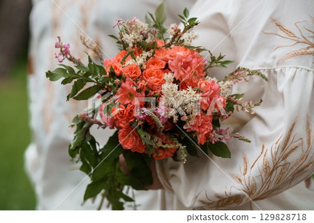 Romantic Bridal Bouquet of Coral Roses and Pink Flowers Held by Bride in White Embroidered Dress, Wedding Day Ceremony. 129828718