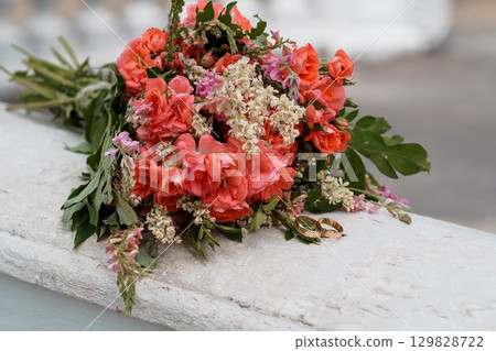 Coral Wedding Bouquet with Rings on Stone Ledge, Romantic Flowers, Celebration, Peach Tones, Bridal Arrangement, Outdoor Ceremony Detail. Coral Wedding Bouquet with Rings on Stone Ledge, Romantic Flowers, Celebration, Peach Tones, Bridal Arrangement, Outdoor Ceremony Detail. 129828722