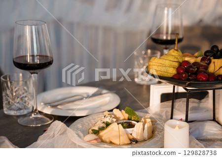 Romantic Wine and Cheese Pairing: Two Glasses, Fruits, Candlelight, Dark Wood Table, Fine Dining, Cozy Atmosphere, Evening Mood. Romantic Wine and Cheese Pairing: Two Glasses, Fruits, Candlelight, Dark Wood Table, Fine Dining, Cozy Atmosphere, Evening Mood. 129828738