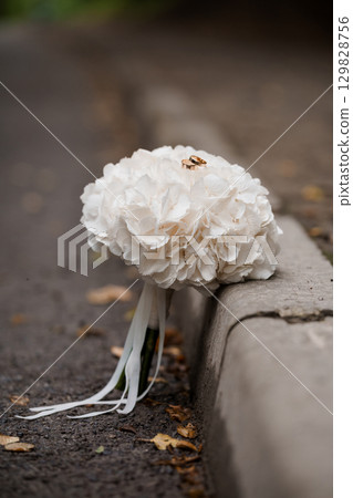 Wedding Rings on White Hydrangea Bouquet Resting on Asphalt Curb, Romantic Scene, Rose Gold Bands, Bokeh, Outdoor Ceremony Details, Soft Focus Wedding Rings on White Hydrangea Bouquet Resting on Asphalt Curb, Romantic Scene, Rose Gold Bands, Bokeh, Outdoor Ceremony Details, Soft Focus 129828756