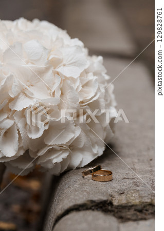 Wedding Rings on Hydrangea: Symbolic Gold Bands Resting Near White Flowers, Elegant Stone Surface, Romantic Celebration. Wedding Rings on Hydrangea: Symbolic Gold Bands Resting Near White Flowers, Elegant Stone Surface, Romantic Celebration. 129828761