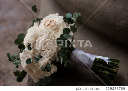 Wedding Rings and White Carnation Bouquet: Romantic Still Life with Eucalyptus, Symbolic Love Token, Elegant Floral Arrangement, Neutral Color Palette 129828769