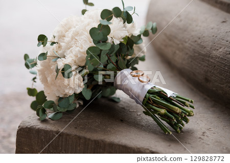 Wedding Bouquet with Gold Rings on Stone Steps, White Flowers, Eucalyptus, Rustic Style, Marriage Symbolism, Ceremony Detail, Natural Light. 129828772