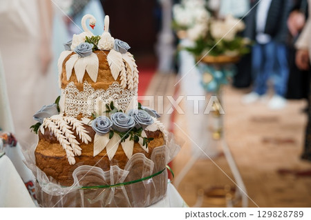 Exquisite Three-Tier Wedding Cake with Swan Topper and Delicate Lace, Decorated with Blue Roses, at Elegant Reception. 129828789