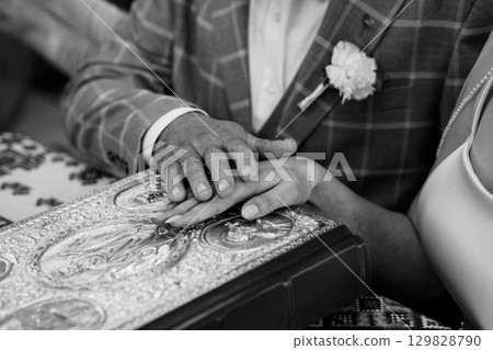 Touching Hands Over Silver Book, Wedding Ceremony, Father and Son, Black and White, Formal Attire, Textured Detail, Emotional Connection. 129828790